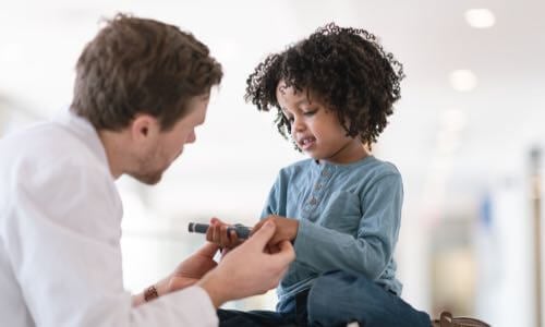 Male health care professional helping a diverse young child with glucose monitoring