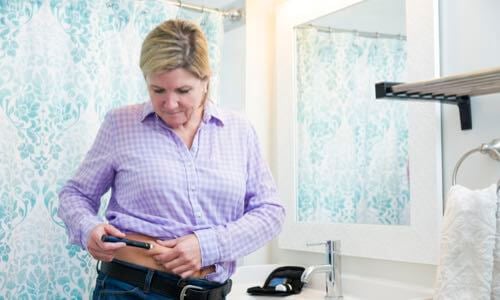 Woman standing at a restroom sink & injecting insulin into her abdomen