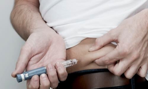 Close-up of a man giving himself an insulin injection in a pinched area of flesh on his abdomen