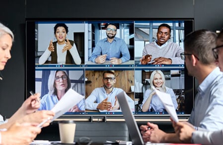 Professionals in conference room viewing large screen virtual meeting