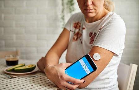 Adult female at a table scans the CGM sensor on her upper arm to get a glucose reading