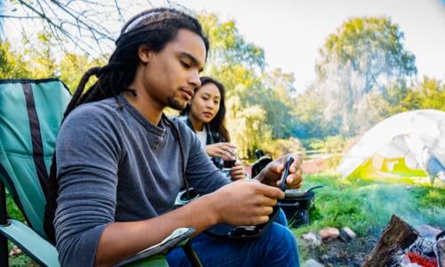 Diverse young man with woman seated outdoors in a campground as he tests his blood sugar level