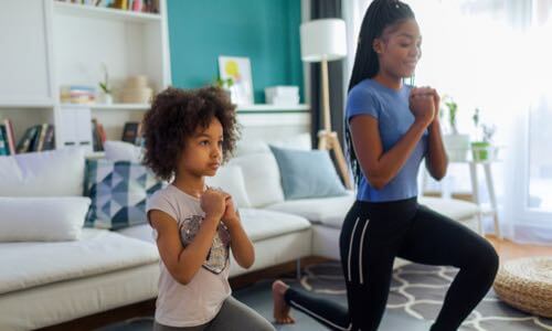 Diverse young mother exercising at home with her young daughter who wears a CGM on her right upper arm