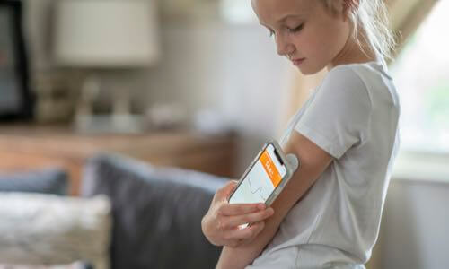 Young girl standing in her living room checking her CGM reading with a smartphone