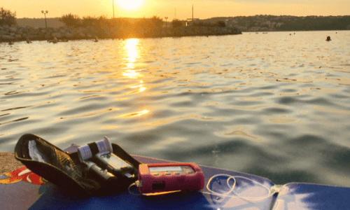 Open diabetes case with an insulin pump on an outdoor table overlooking a lake at sunset