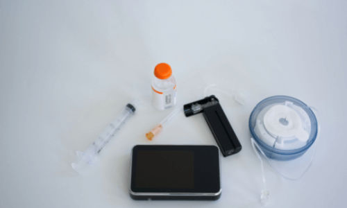 Insulin pump, cartridge refill, insulin bottle, syringe, infusion set & applicator laying on a table