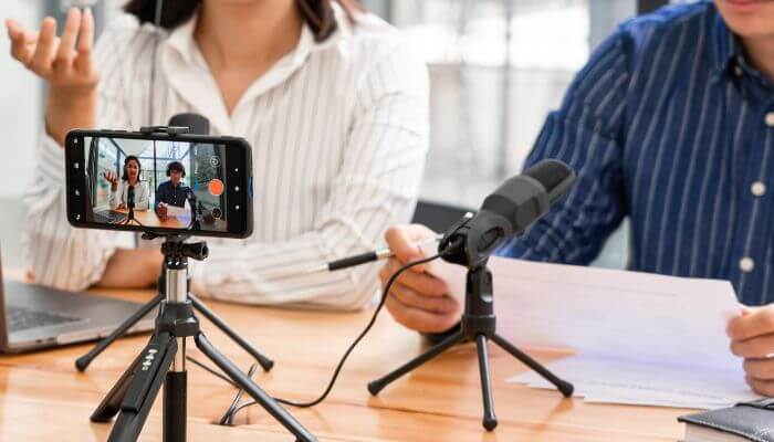 Smartphone video recording of male & female sitting at desk & speaking into microphone
