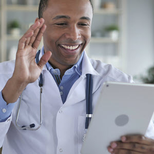 Male healthcare provider smiling & waving at a tablet