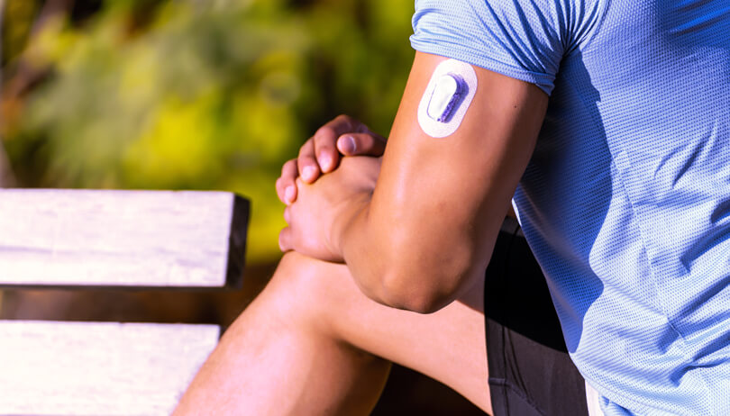 Close-up of physically fit male stretching outdoors & wearing a CGM on his upper arm